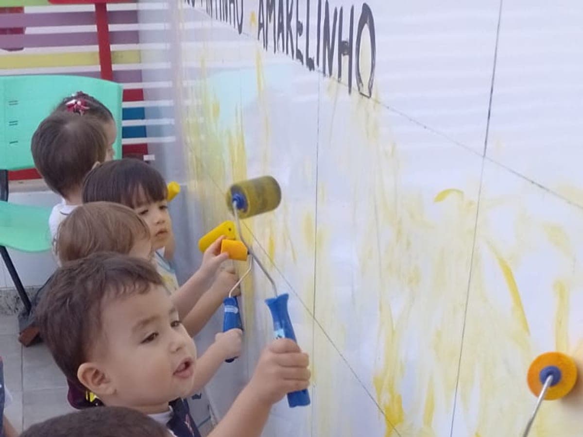 Crianças pequenas pintando um painel branco com rolinhos de tinta amarela