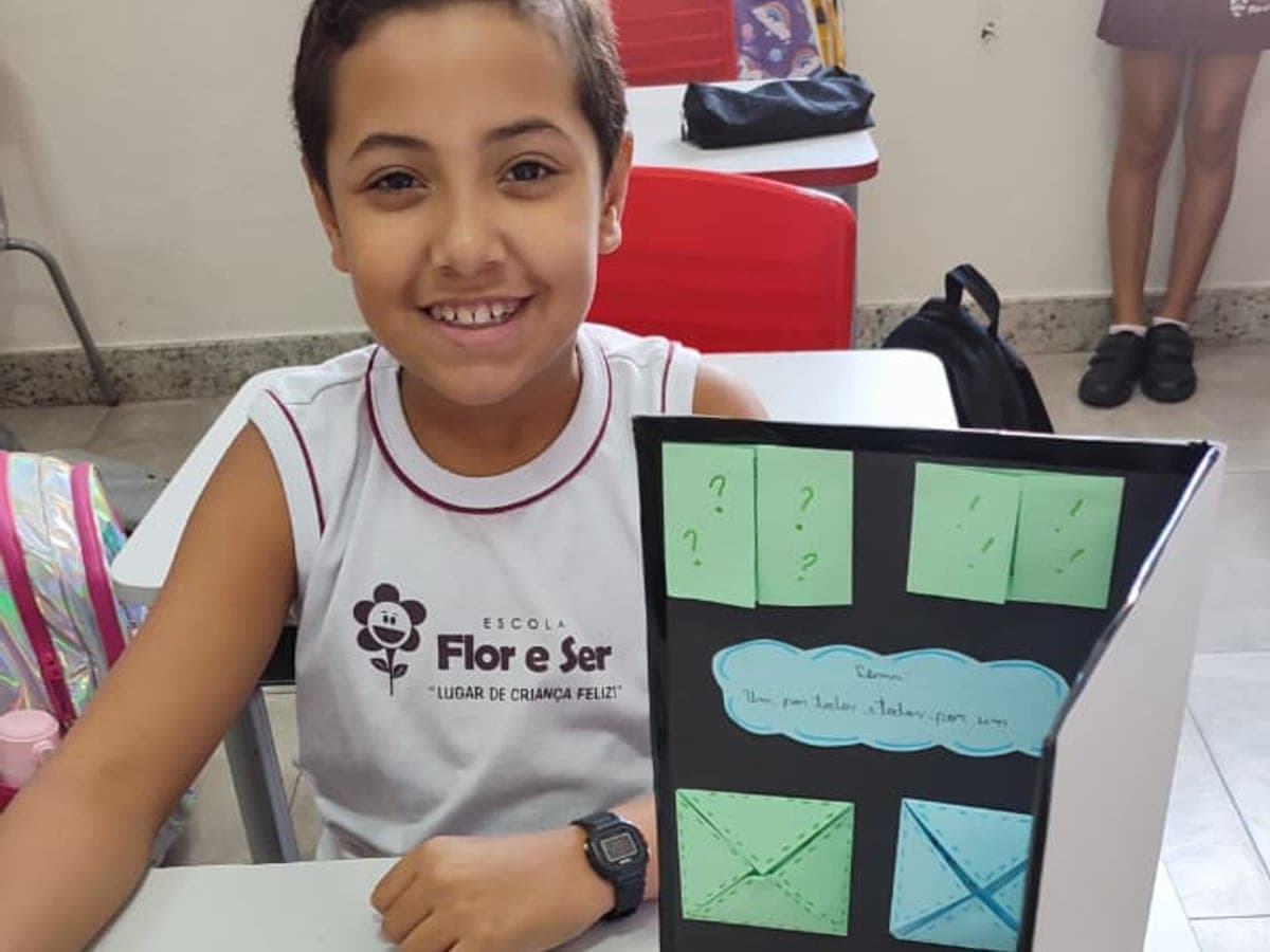 Aluno do fundamental sorrindo ao lado do cartaz do seu projeto